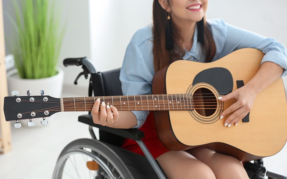 Young female musician in wheelchair playing guitar at home
